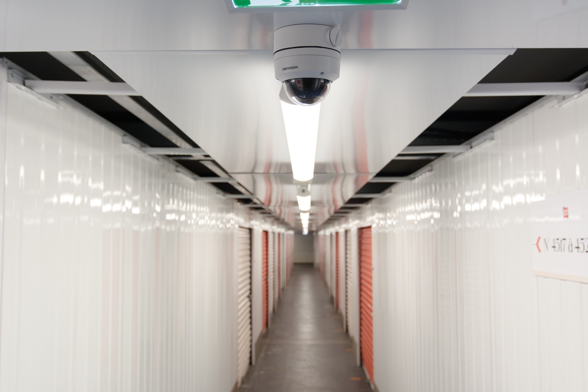 Long couloir intérieur de boxes avec caméra dôme et néons au plafond, HOMEBOX Béthune
