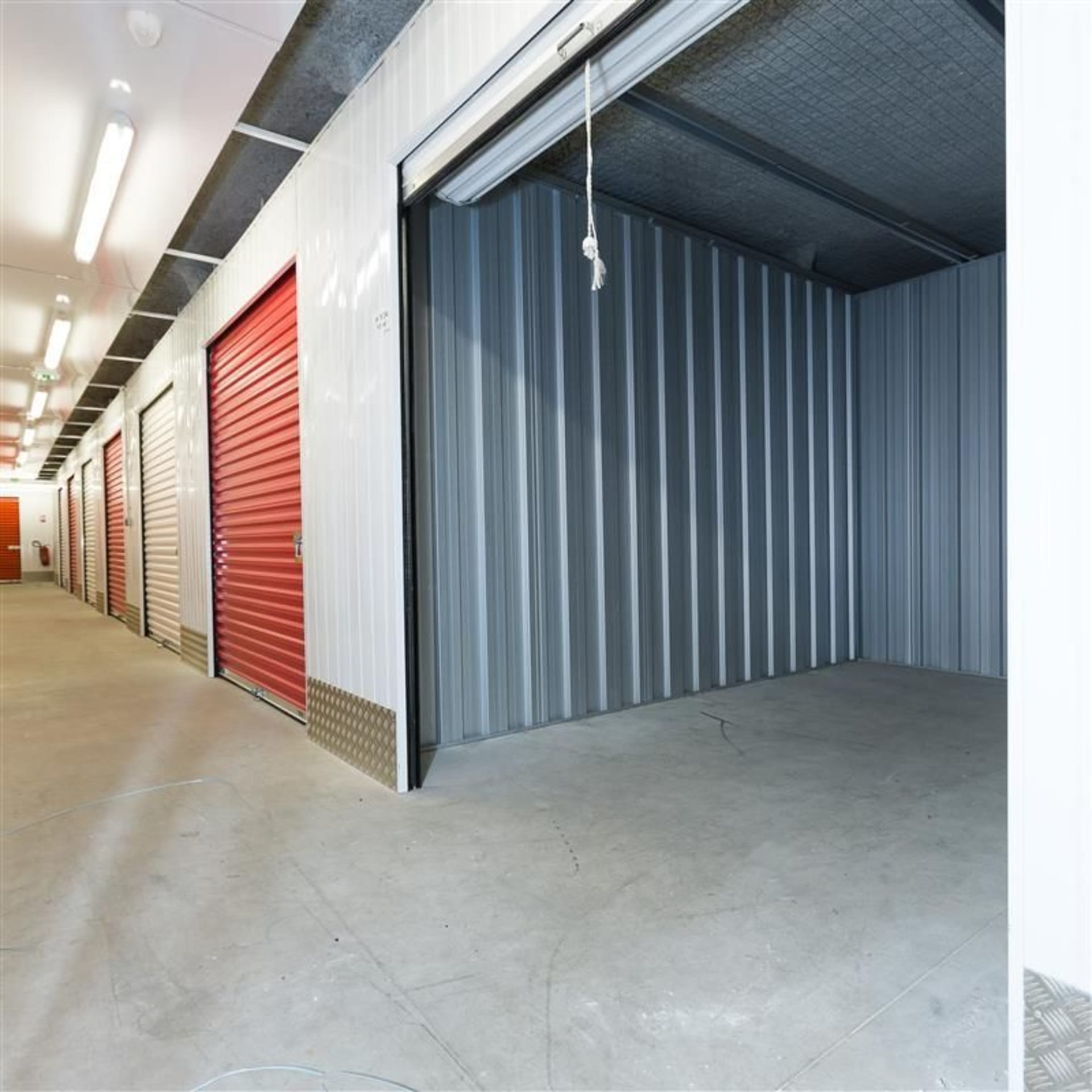 Couloir intérieur avec porte de box rouge ouverte et cellule vide, HOMEBOX Mont-de-Marsan