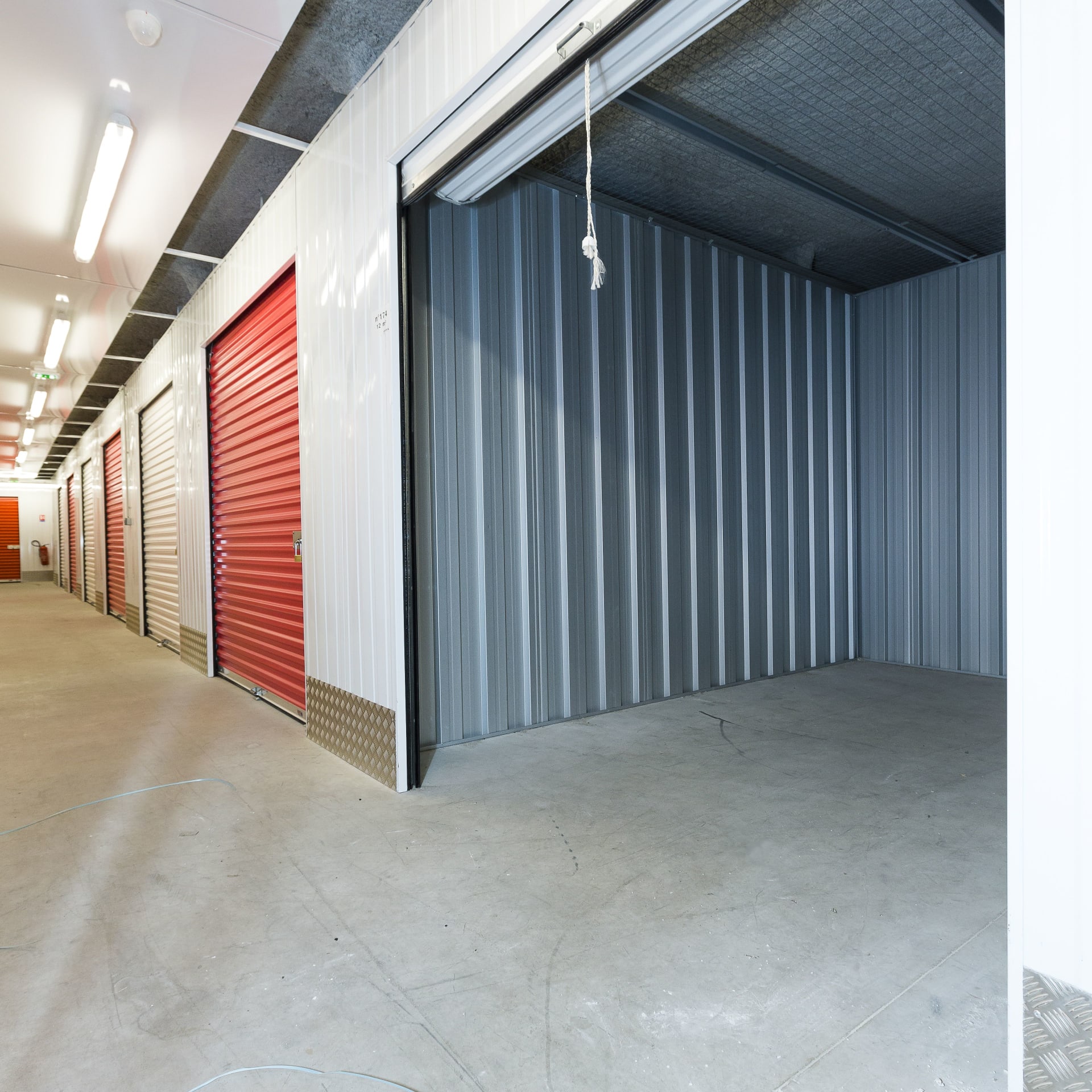 Indoor corridor with red and white storage unit doors and open empty box at HOMEBOX Angoulême La Couronne