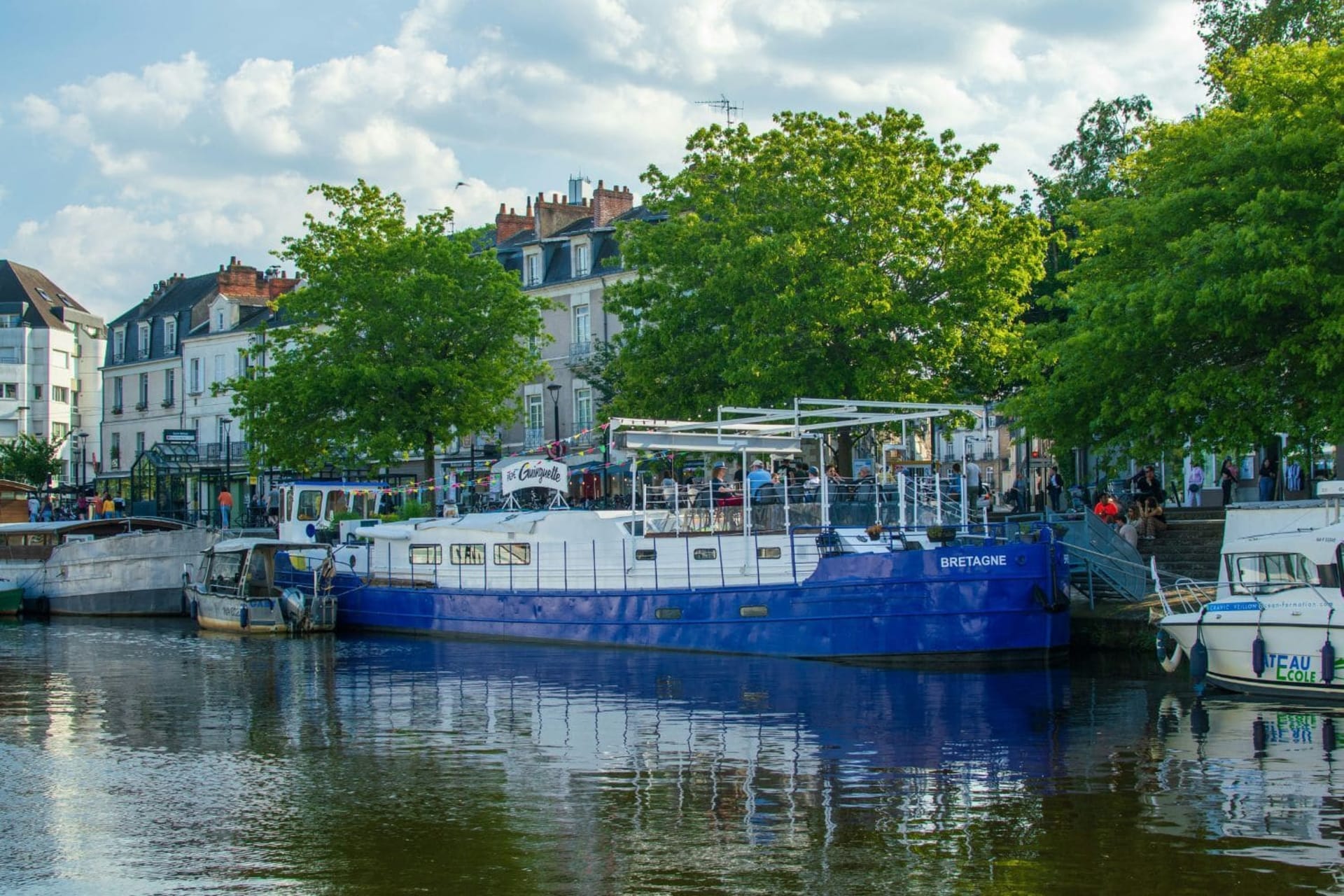 Péniche blanche et bleue sur l’Erdre, grands arbres feuillus derrière