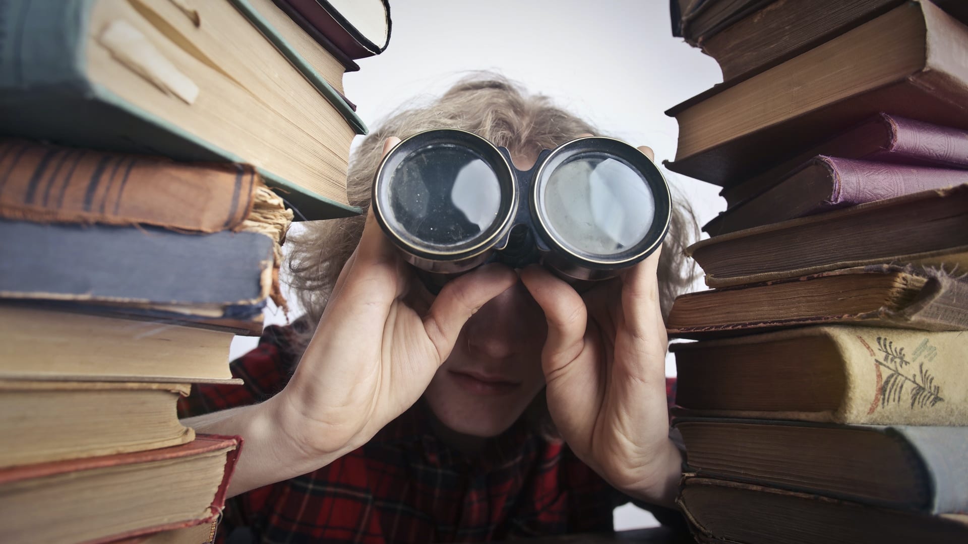 He or she in between columns of books is zooming with binoculars