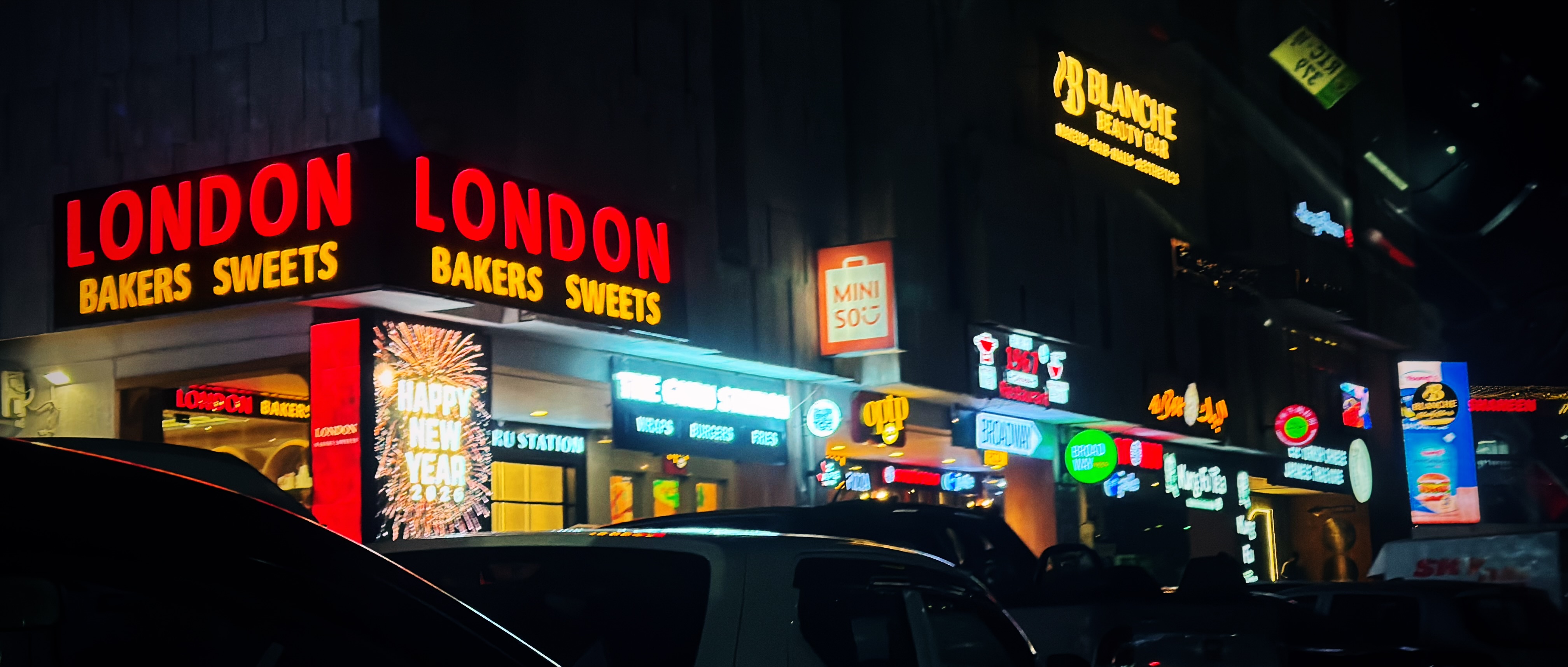 a nighttime photo of shops on a corner with cars reflecting on their outline