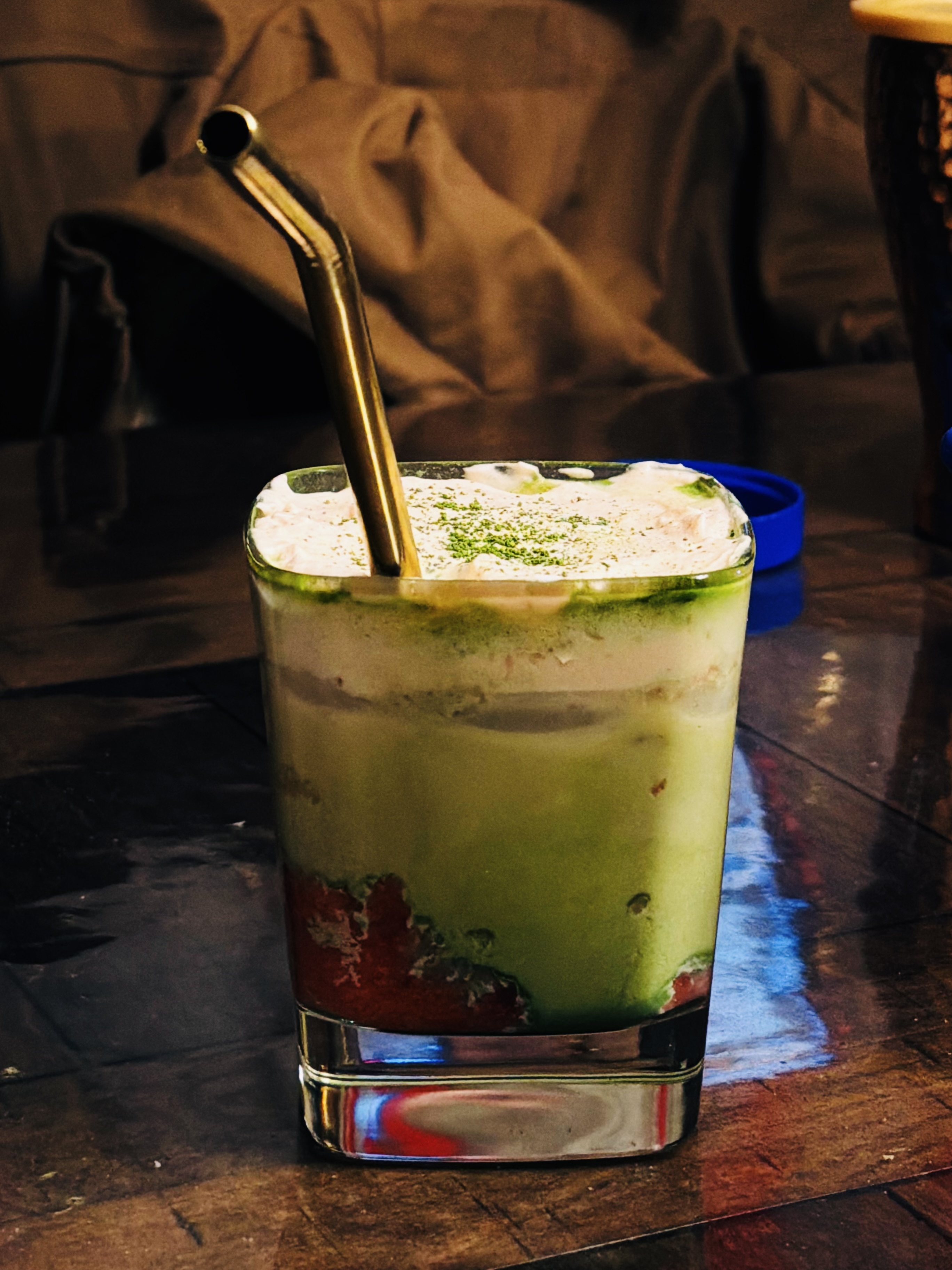 a green and red cup with a golden straw emerging from the top on a wooden table