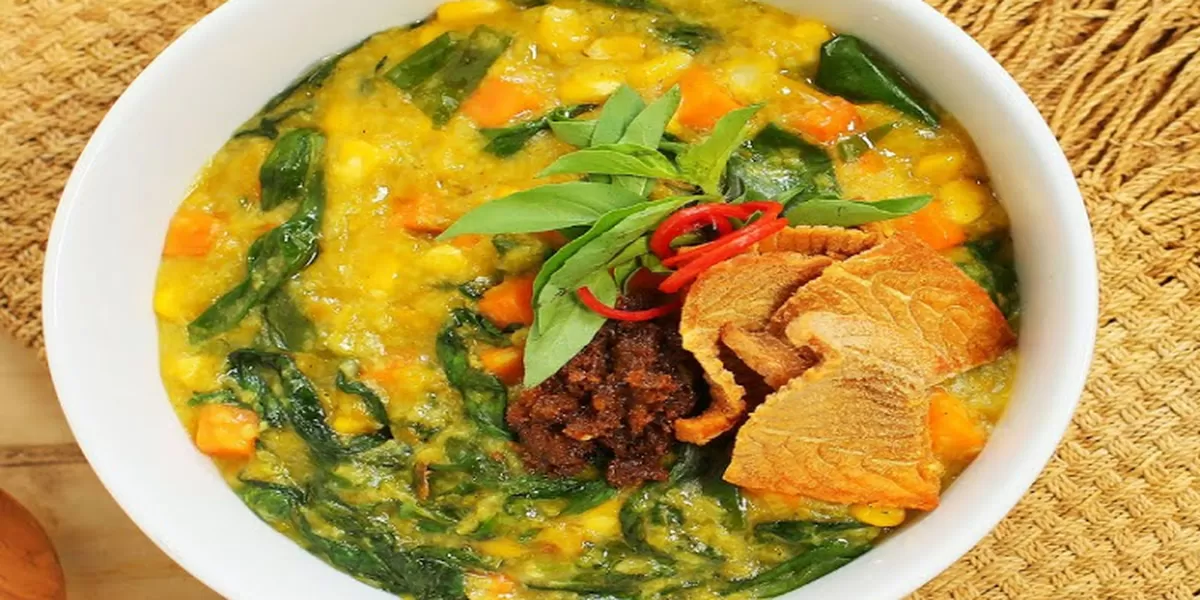 Tinutuan atau Bubur Manado — semangkuk bubur kuning kental dengan potongan sayuran bayam, labu, jagung, dan kangkung yang disajikan hangat dengan sambal dan ikan asin