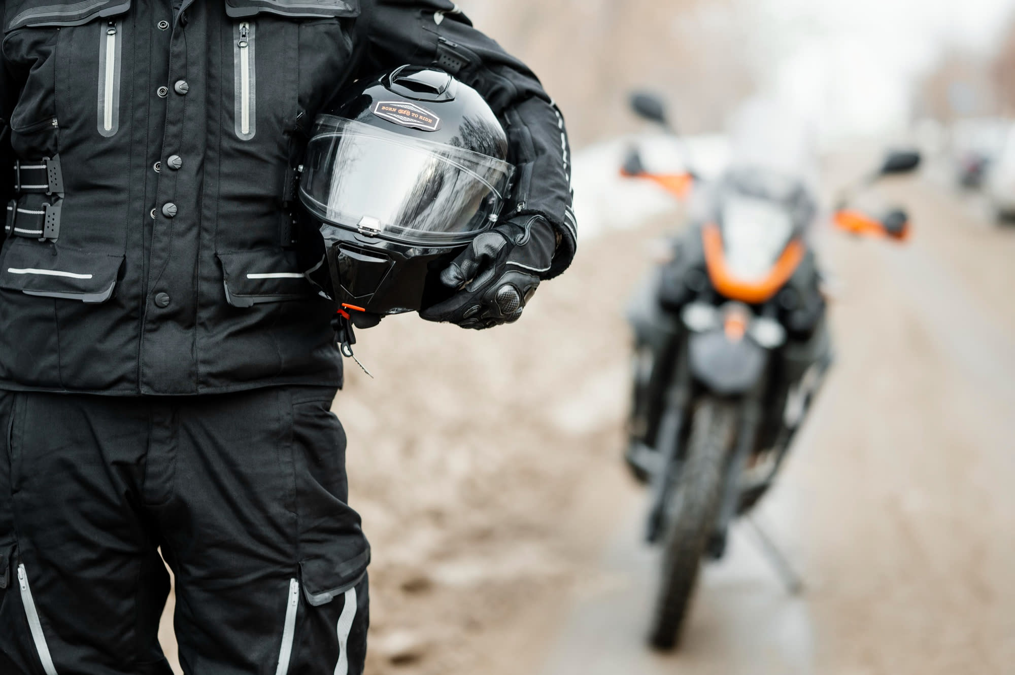 Close-up of a rider in full safety gear (helmet, armored jacket, gloves) preparing to ride with Thai mountains in the background