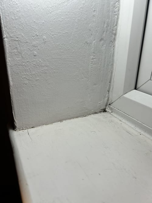 A window reveal and sill with rough paintwork and an open joint between them