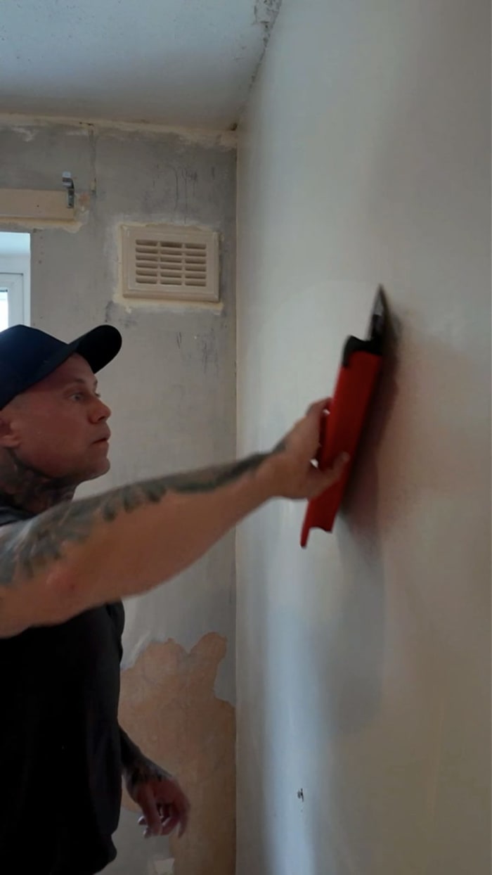 Roller filler being skimmed flat across the wall with a red trowel