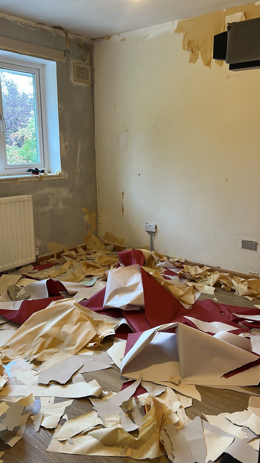 The bedroom part way through stripping, with red and cream paper covering the floor and the walls back to bare render