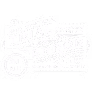 Trial & Error logo rendered in white, featuring a vintage-style badge design with 'Hand Crafted' and 'Small Batch' text.