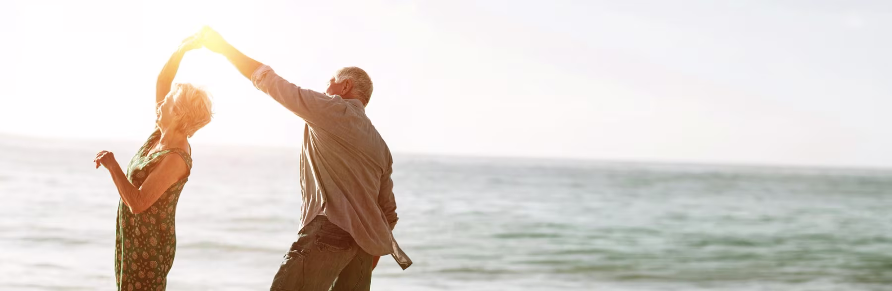 A senior couple dancing together on a beach at sunset
