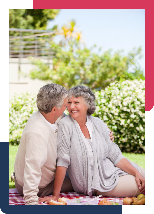 A man and woman in their seventies laughing together over a picnic in a garden