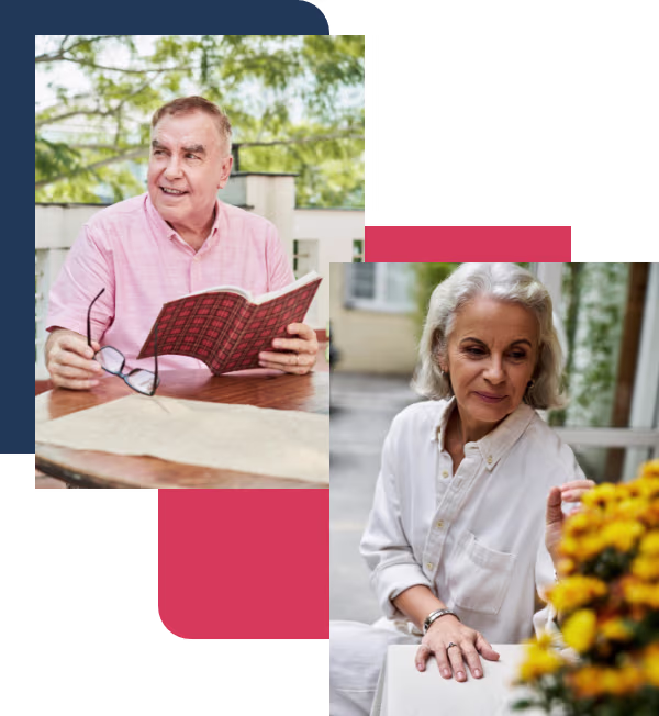 A smiling man in his sixties reading a book at an outdoor table, and a silver-haired woman sitting beside yellow flowers