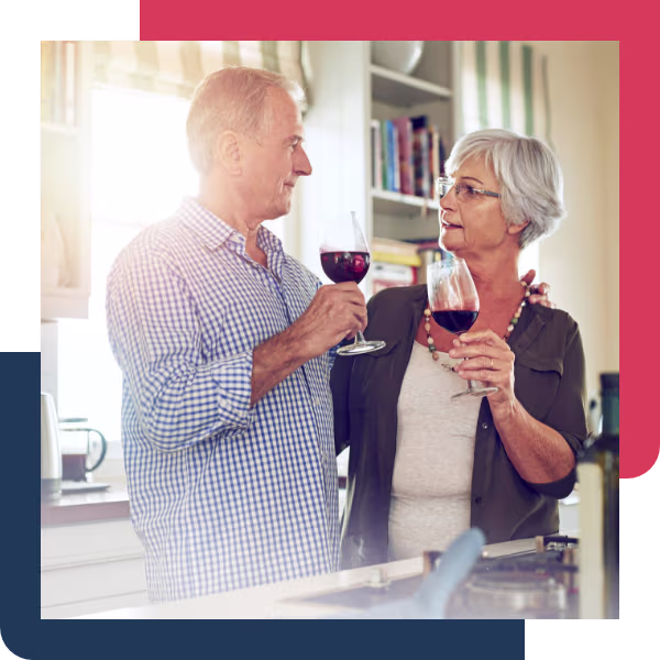A man and woman in their sixties sharing a glass of red wine in a sunlit kitchen