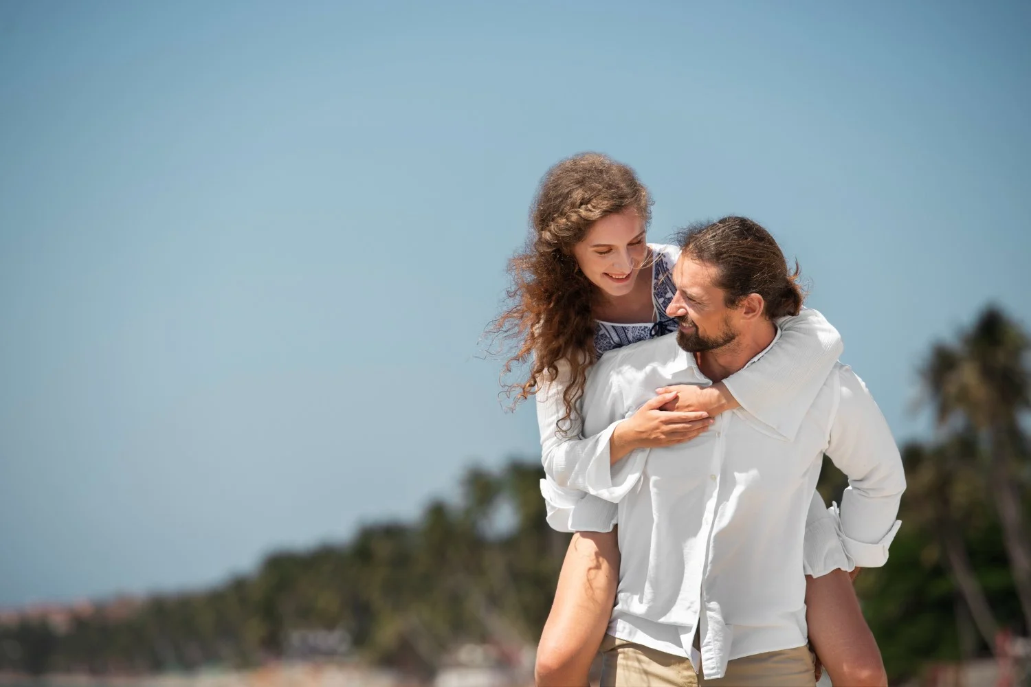 Man and woman under a clear blue sky, both smiling joyfully