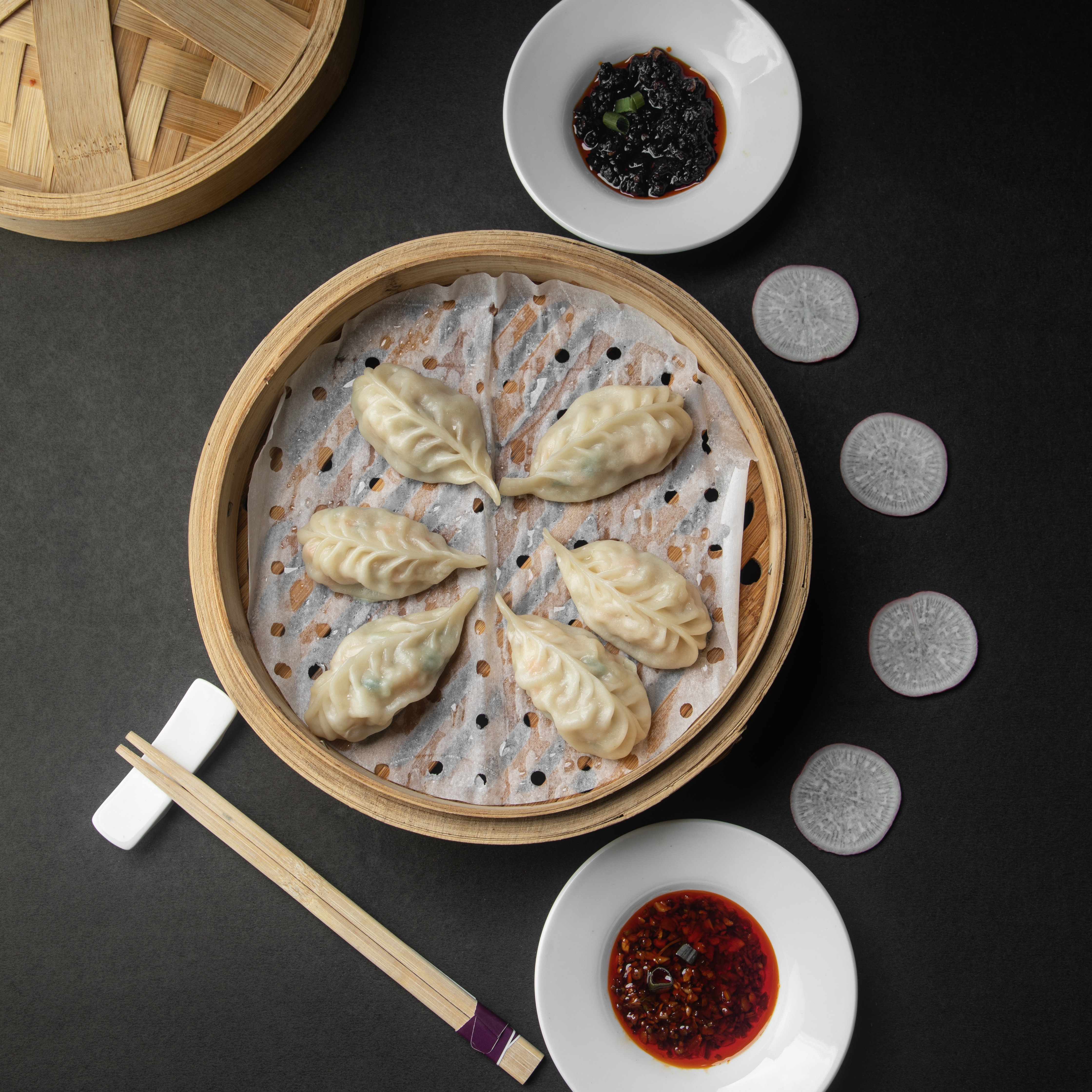 A hand-folded dim sum basket steaming on a black stone table
