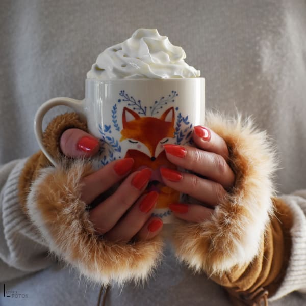 Chocolat chaud avec chantilly dans une tasse renard tenue par des mains avec mitaines en fourrure