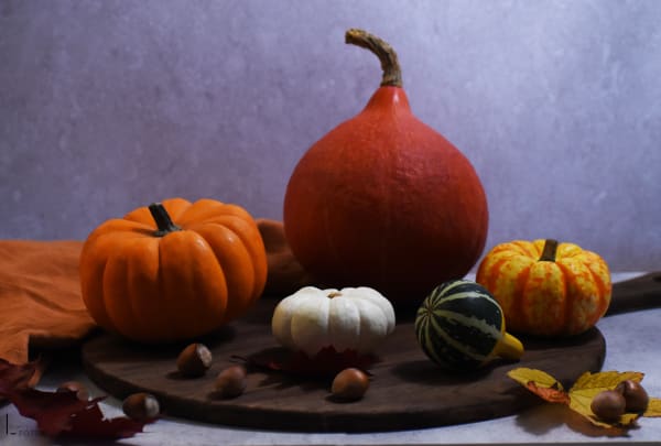 Composition automnale de courges et citrouilles variées sur planche en bois avec noisettes et feuilles mortes