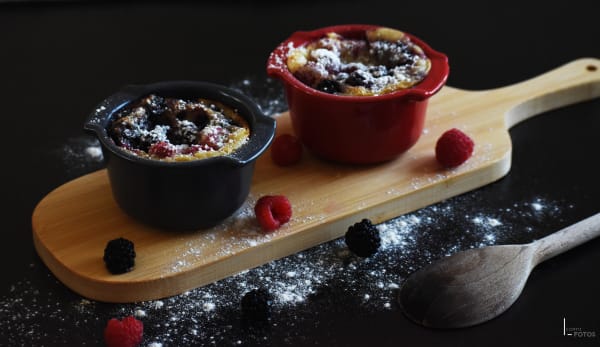 Mini clafoutis aux framboises et mûres en cocottes, saupoudrés de sucre glace sur planche en bois