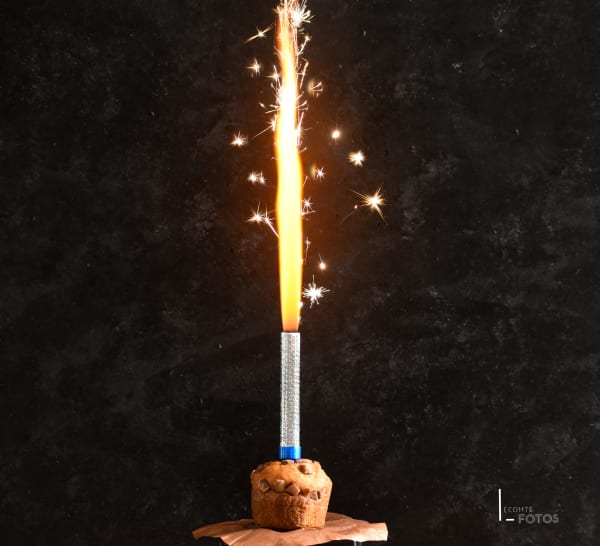 Muffin au chocolat avec fontaine d'étincelles allumée projetant des gerbes lumineuses sur fond noir