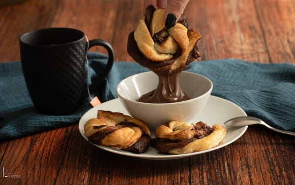 Brioches torsadées au chocolat trempées dans un bol de chocolat fondu sur table en bois