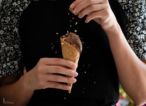 Cornet de glace au chocolat saupoudré d'éclats de fruits secs, tenu à la main sur fond sombre