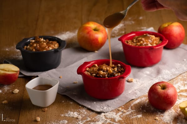 Trois mini cocottes de crumble aux pommes avec caramel versé à la cuillère, pommes et farine sur table en bois