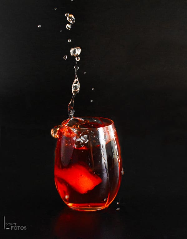 Verre tumbler de cocktail rouge vif avec glaçons et éclaboussures suspendues en l'air sur fond noir