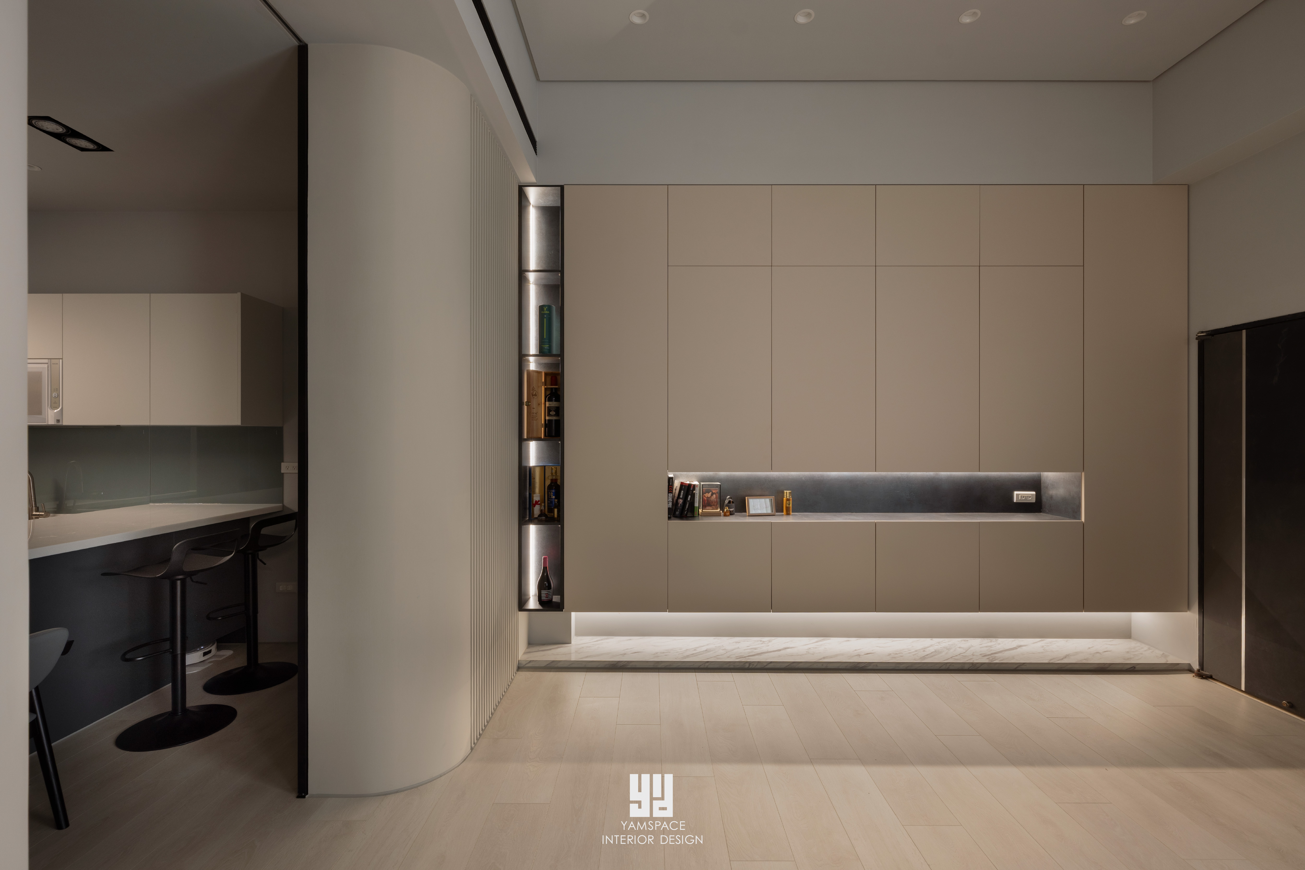 神岡透天舊屋翻新｜現代仛寂風：客廳通往餐廚的過渡區採大角度圓弧立面收口，搭配長條型嵌入式壁龕展示槽與隱藏照明，整合動線並保留視覺通透感。
