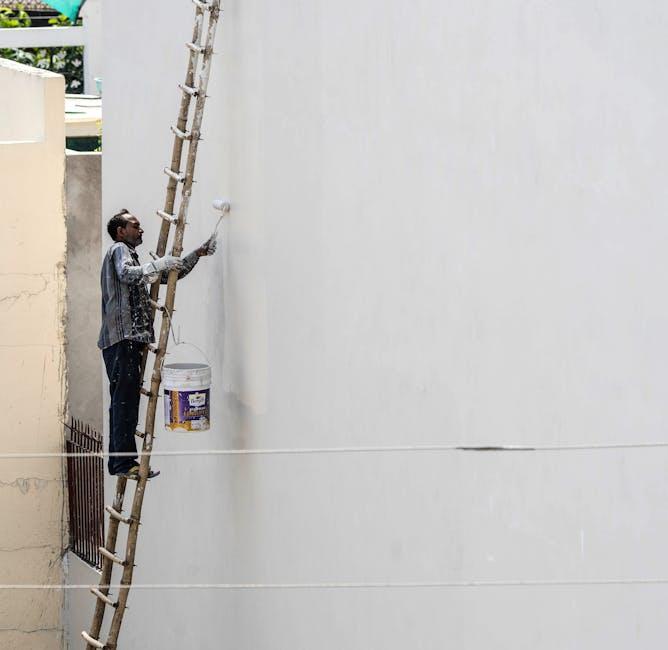 A painter on a ladder painting the exterior wall of a white house