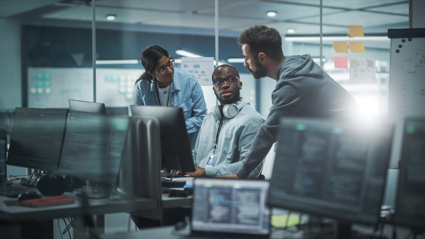 a team of three in the office discussing in front of the computer
