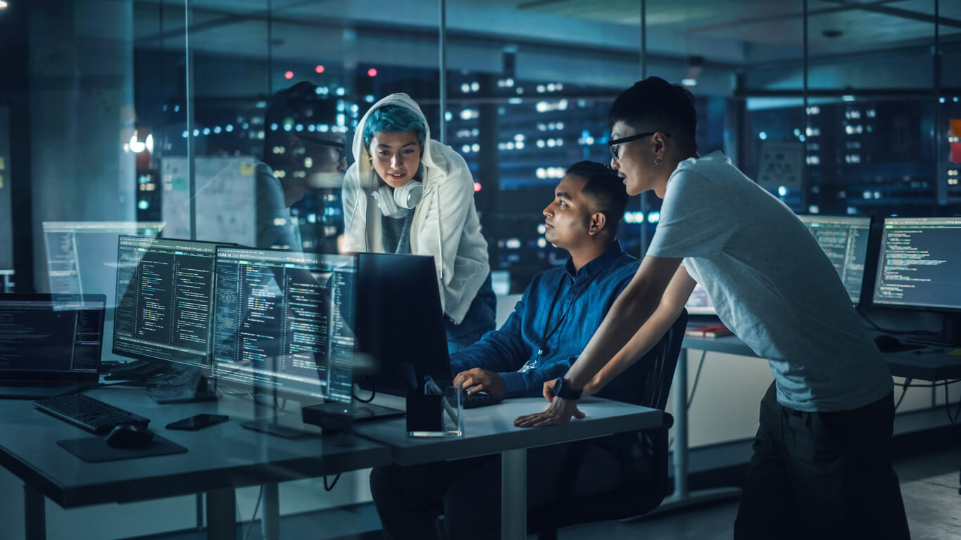  Red team of three people sitting in the office in front of computer and chatting