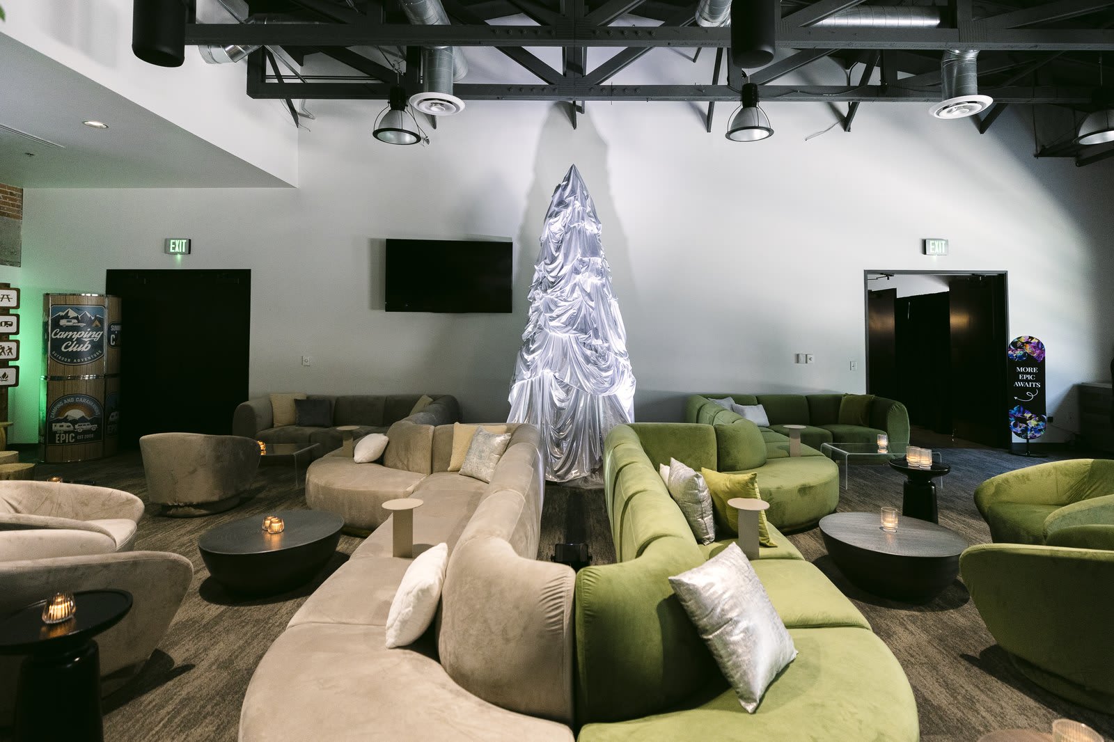Holiday lounge with curved moss green and ivory velvet sofas, white and silver pillows and a white sparkling Christmas tree