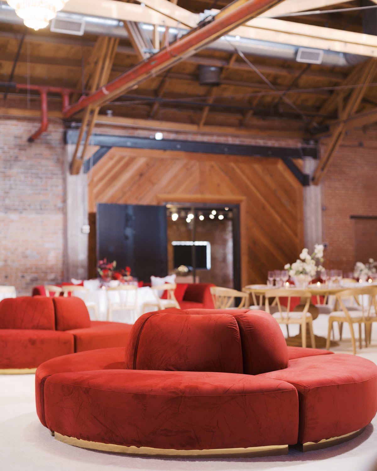 Round crimson velvet sofa with a center backrest in a warehouse venue set for a holiday party