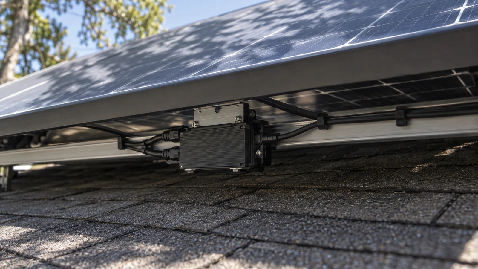 Compact module-level microinverter mounted beneath a residential rooftop solar panel