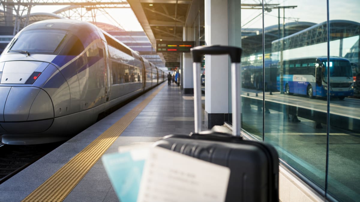 Black suitcase on a station platform beside a high-speed train and a bus