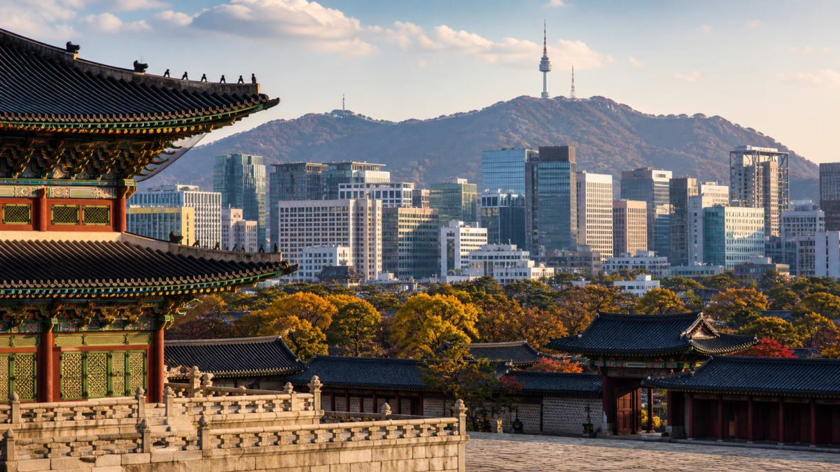 Traditional palace rooftops with Seoul skyline and Namsan Tower behind at sunset