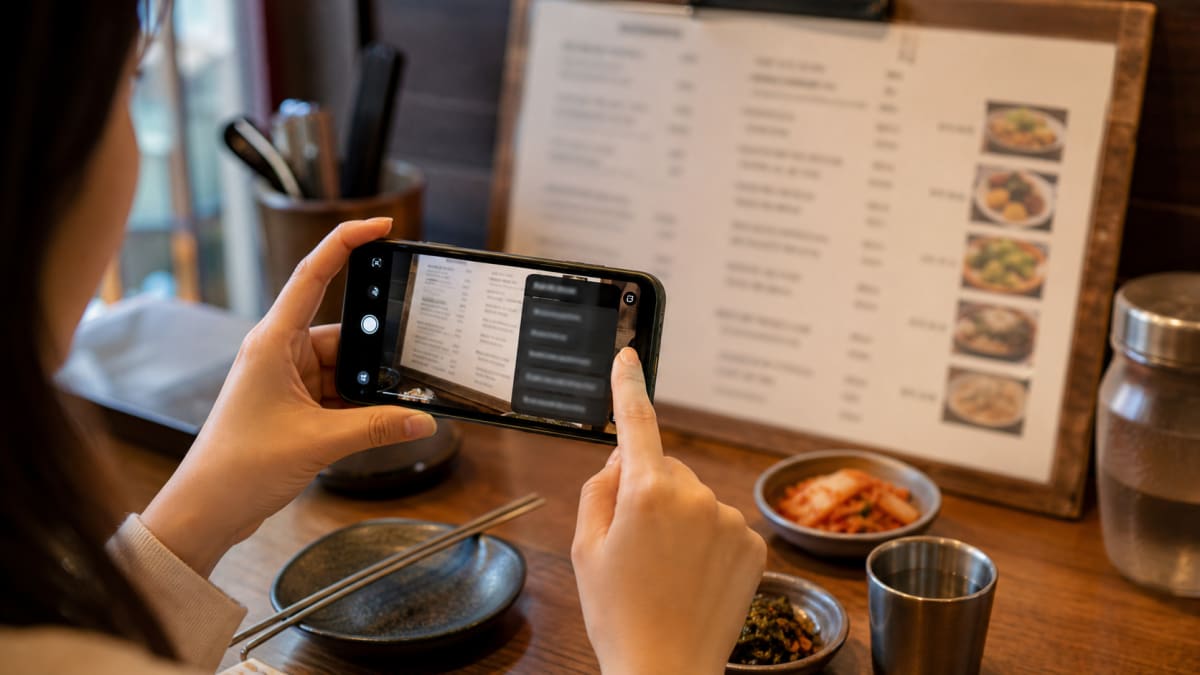 Hand holding a phone using camera translation on a printed Korean menu