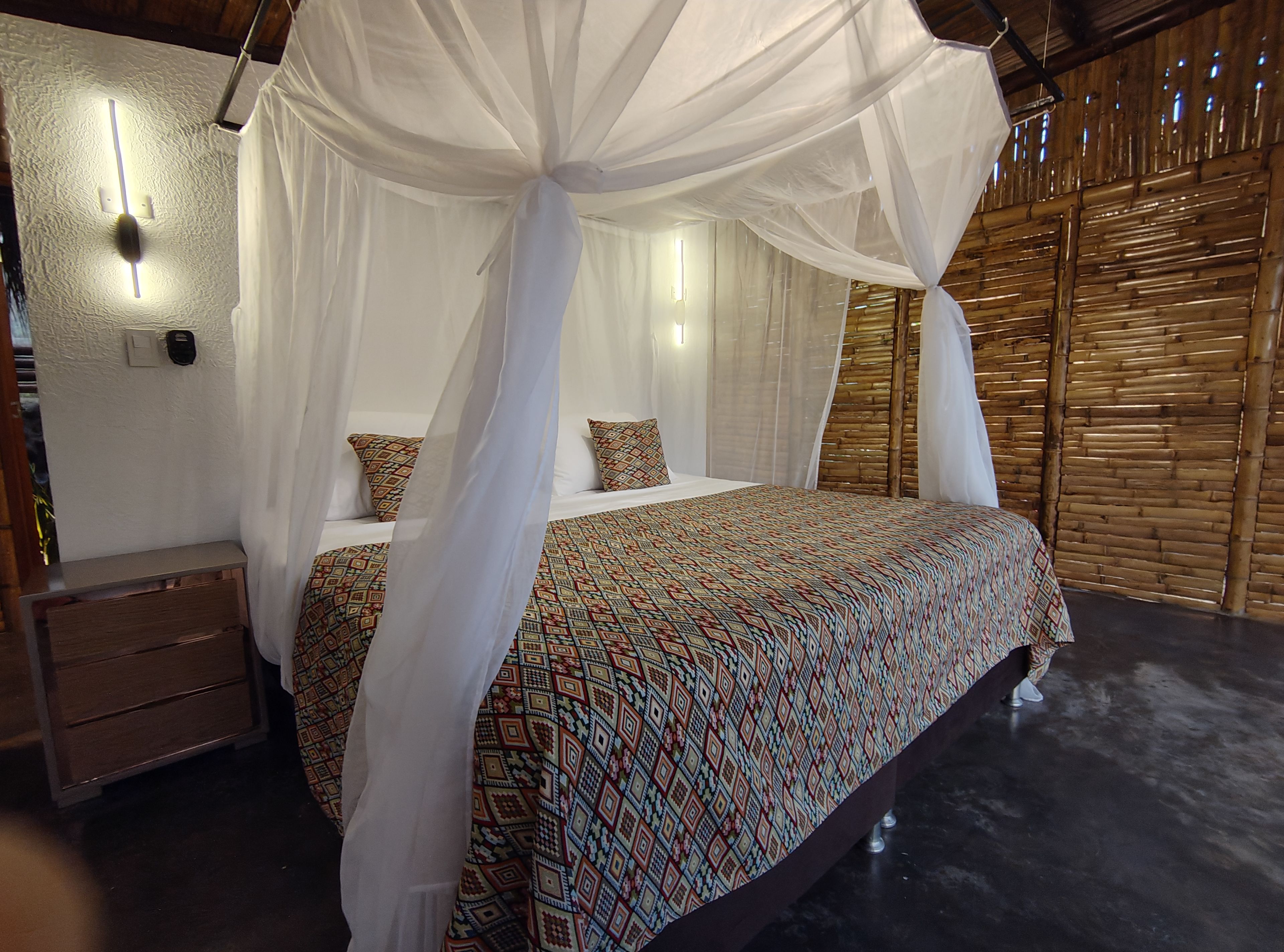 Cama king con mosquitero blanco, cobija artesanal de colores y paredes de bambú