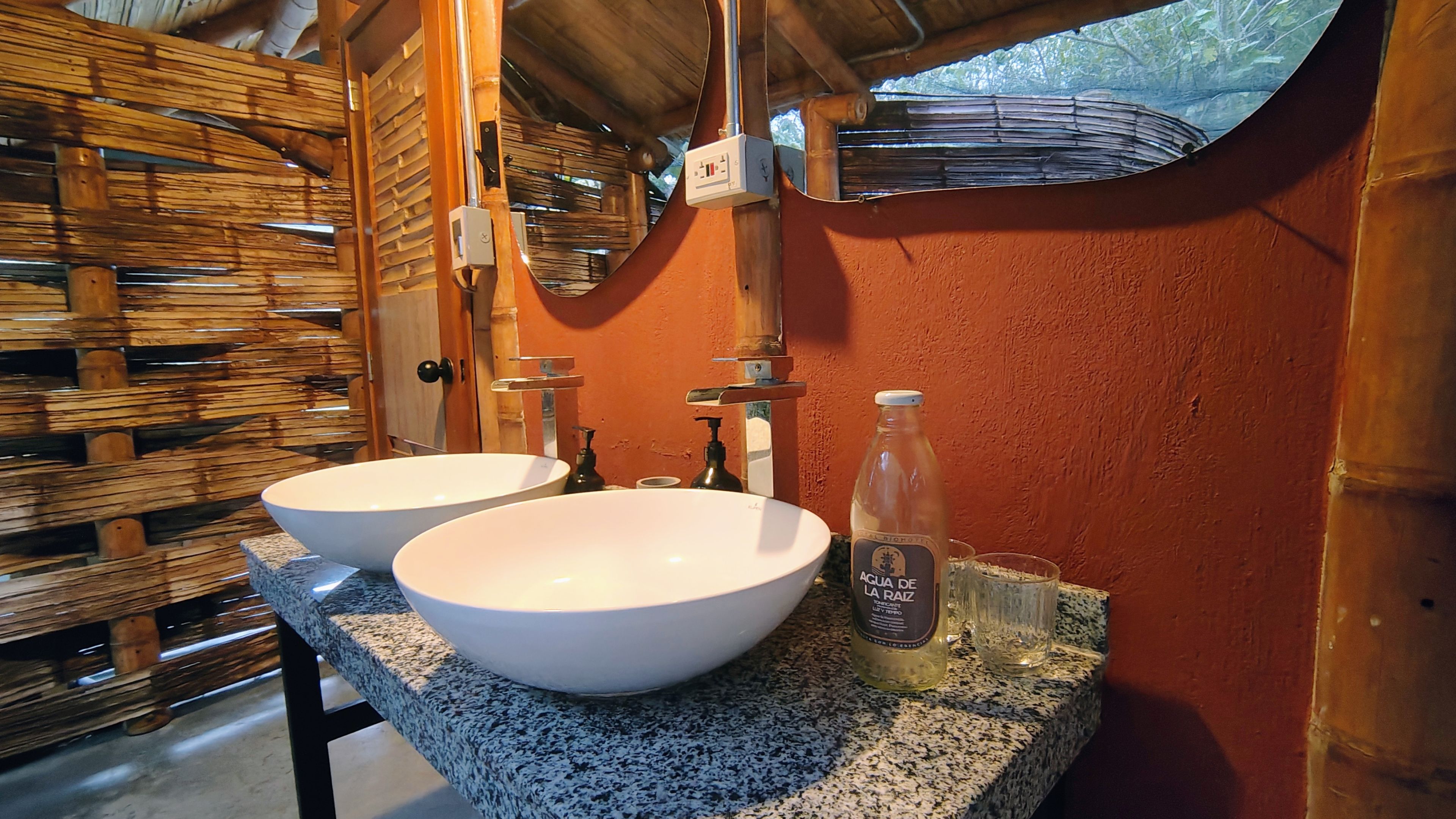 Baño con doble lavamanos de piedra y pared naranja terracota