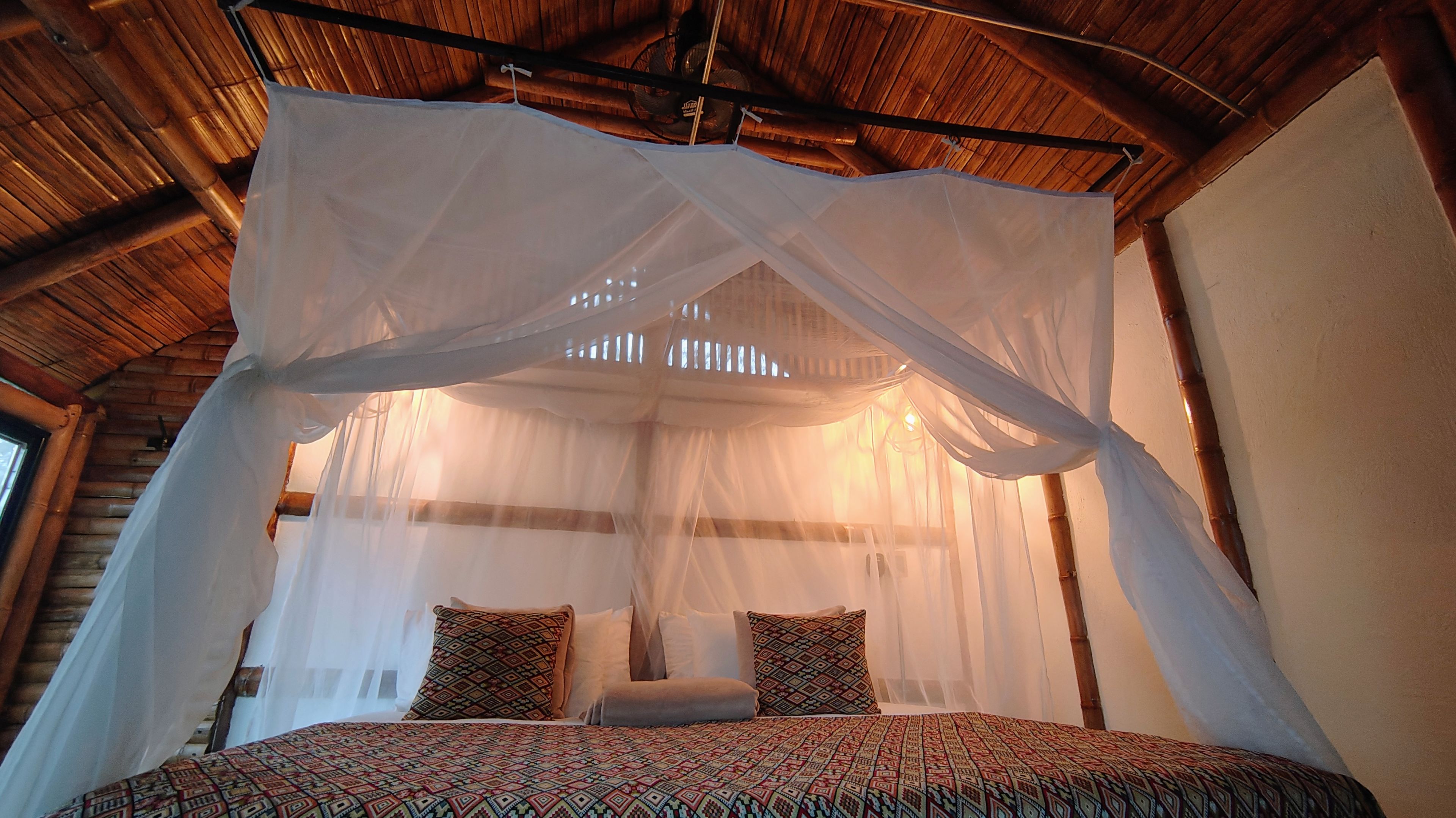 Cama king con mosquitero blanco y techo de bambú en la Suite Río