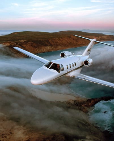 Cessna Citation CJ1 in flight above clouds near a coastal shoreline