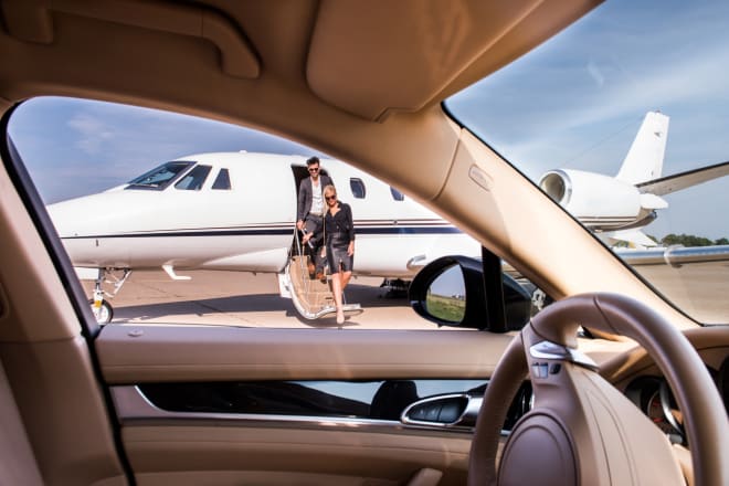 A couple departing a private jet as seen from inside a waiting luxury vehicle