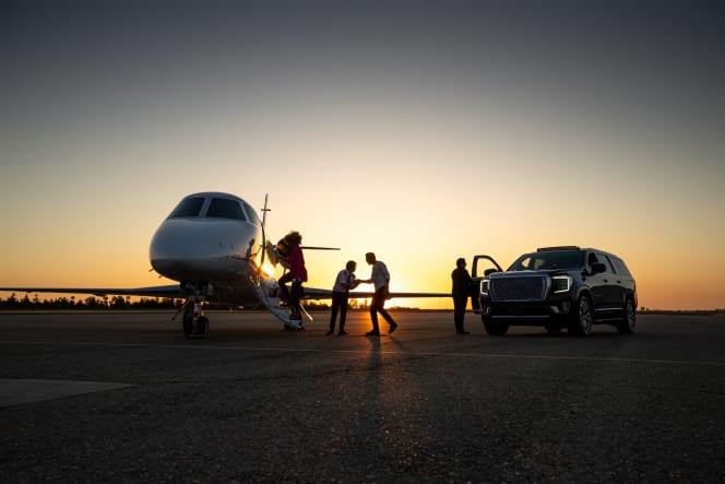 Passengers departing a private jet at sunset alongside a luxury SUV on the tarmac