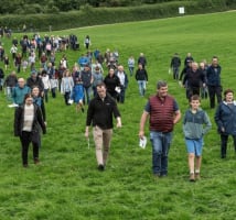 People of various ages walking through a grassland field as part of a farm walk