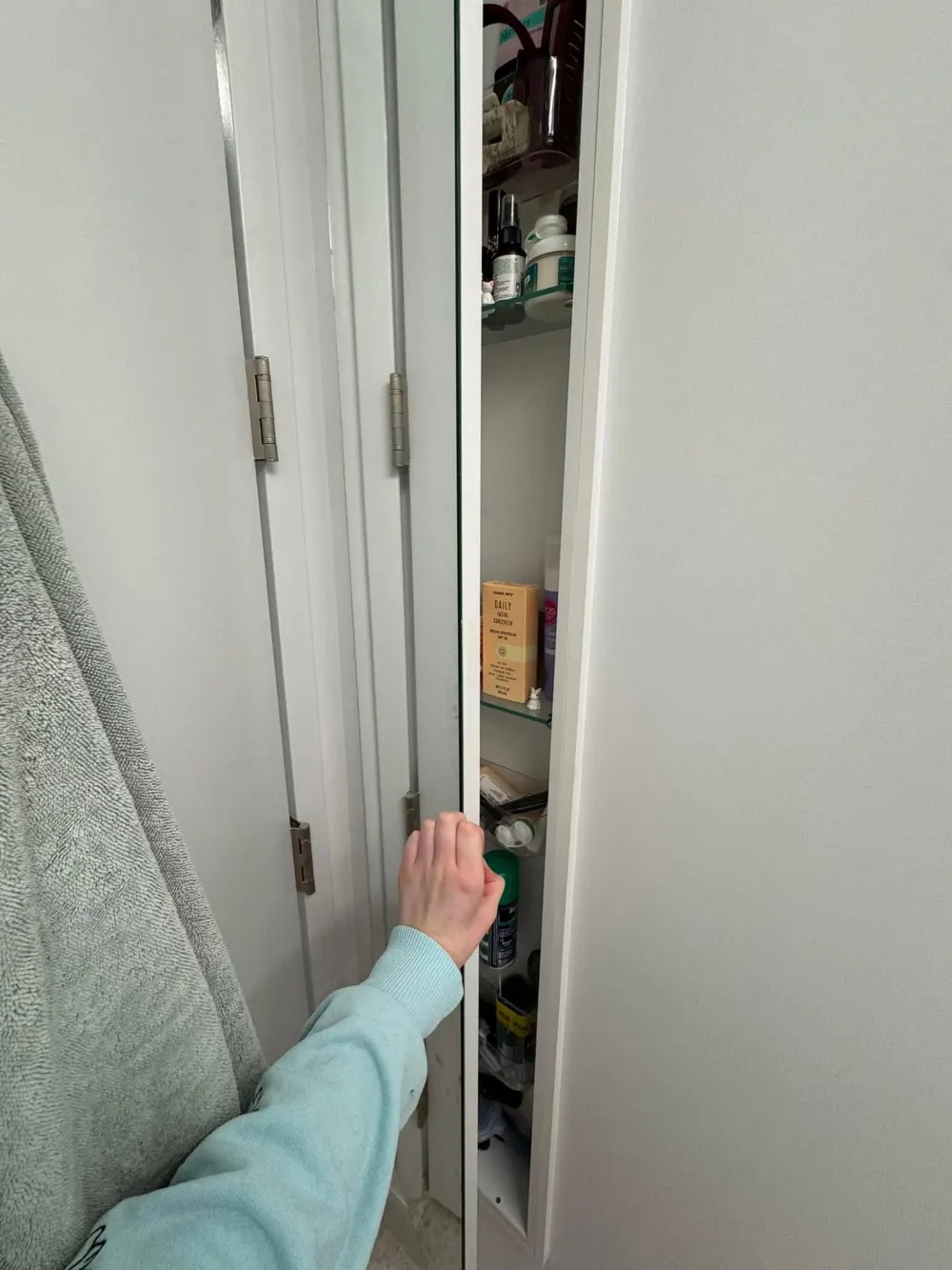 Hand opening a bathroom cabinet.