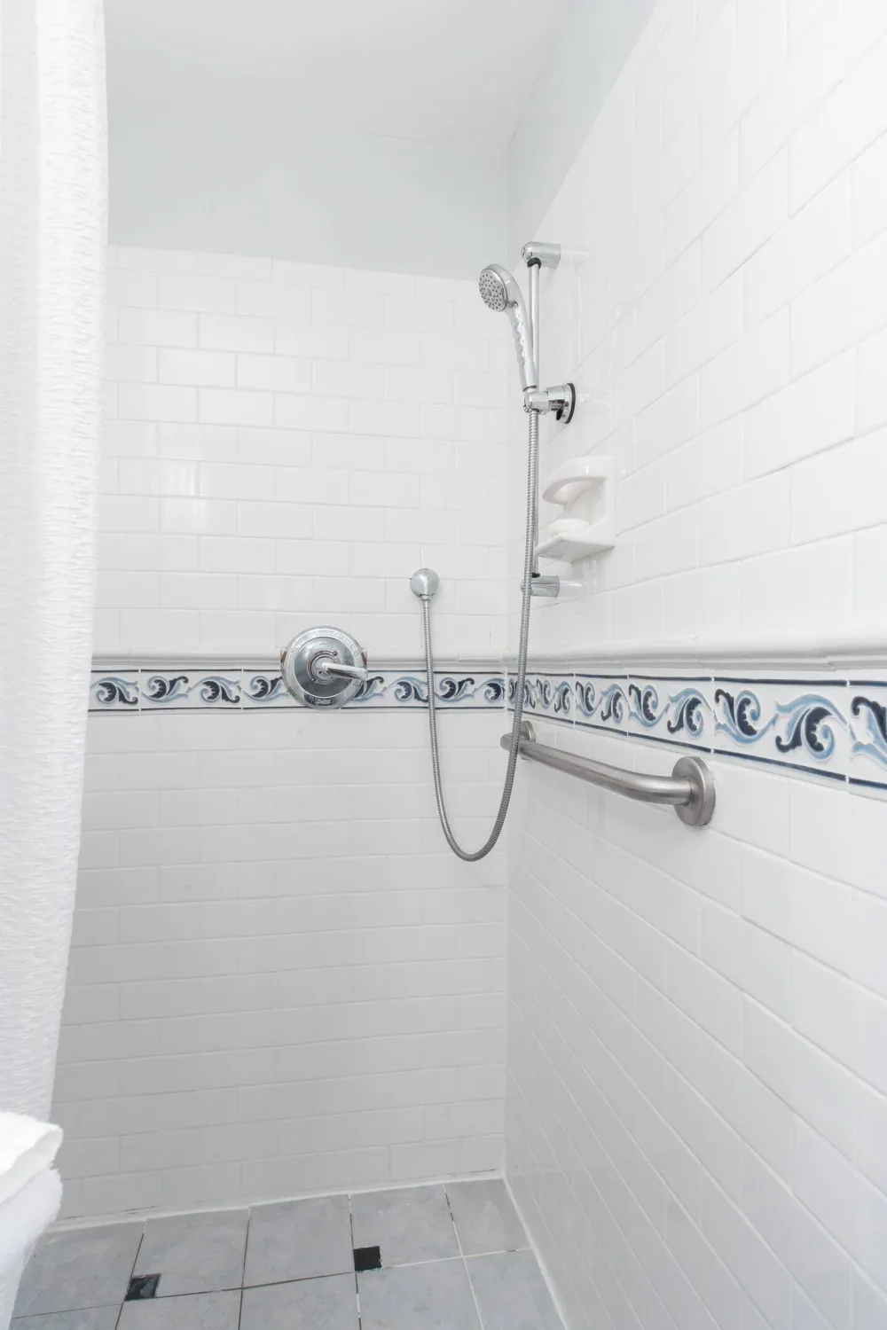 White tiled shower with railing.