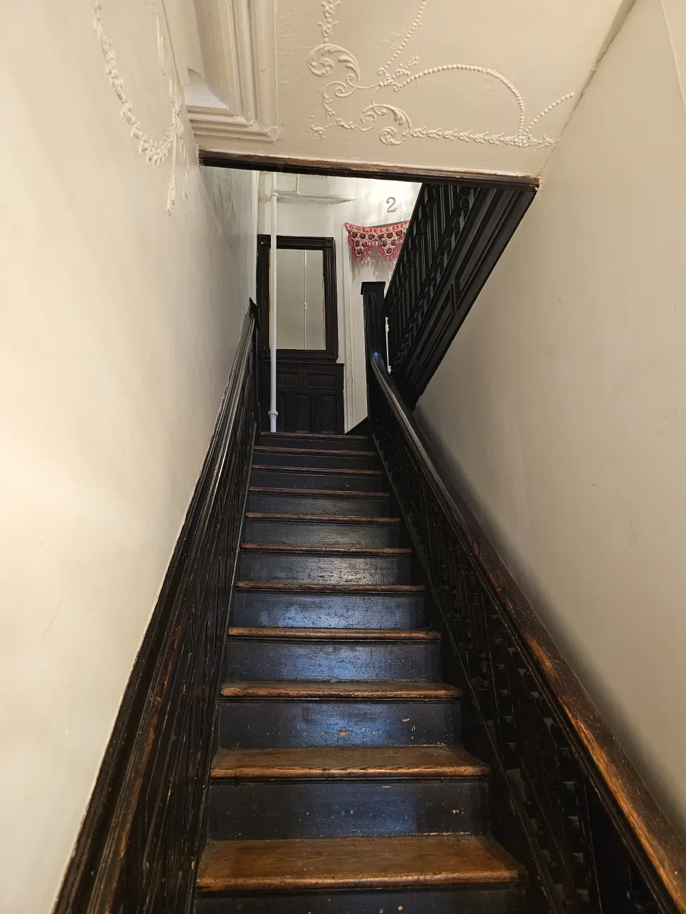 Narrow wooden staircase with ornate ceiling.