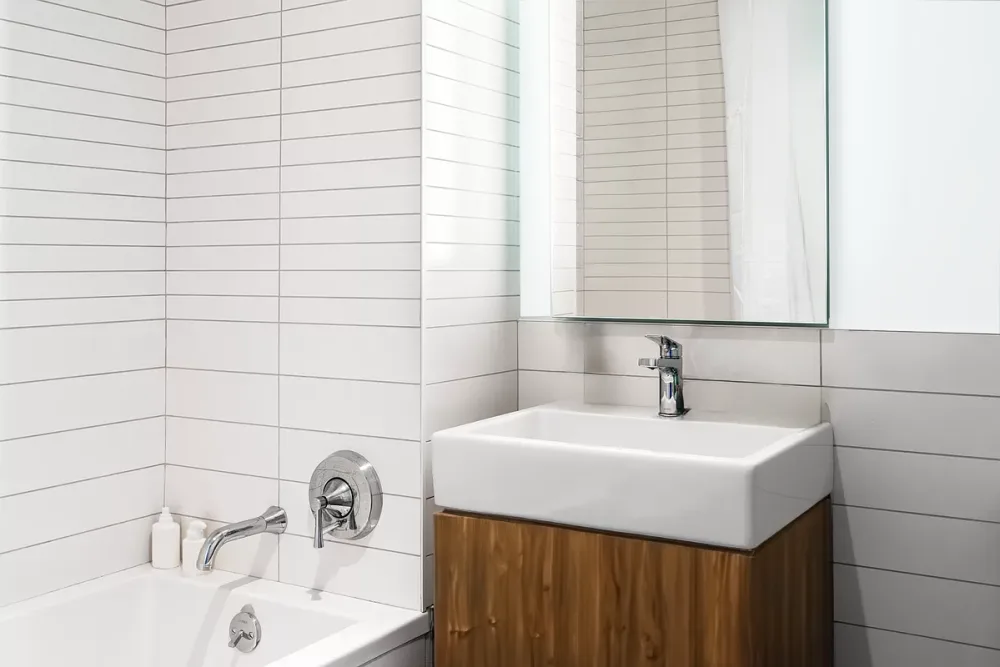Modern, white-tiled bathroom with bathtub.