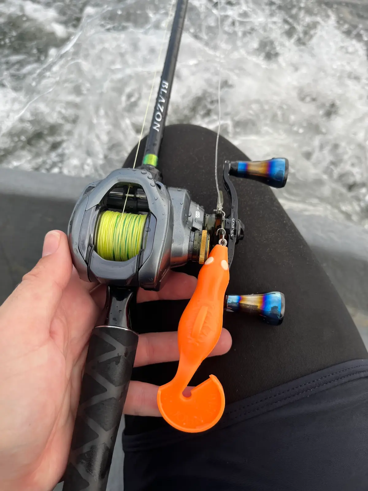 Orange soft plastic swimbait attached to a baitcasting setup in a boat while fishing Thailand freshwater.