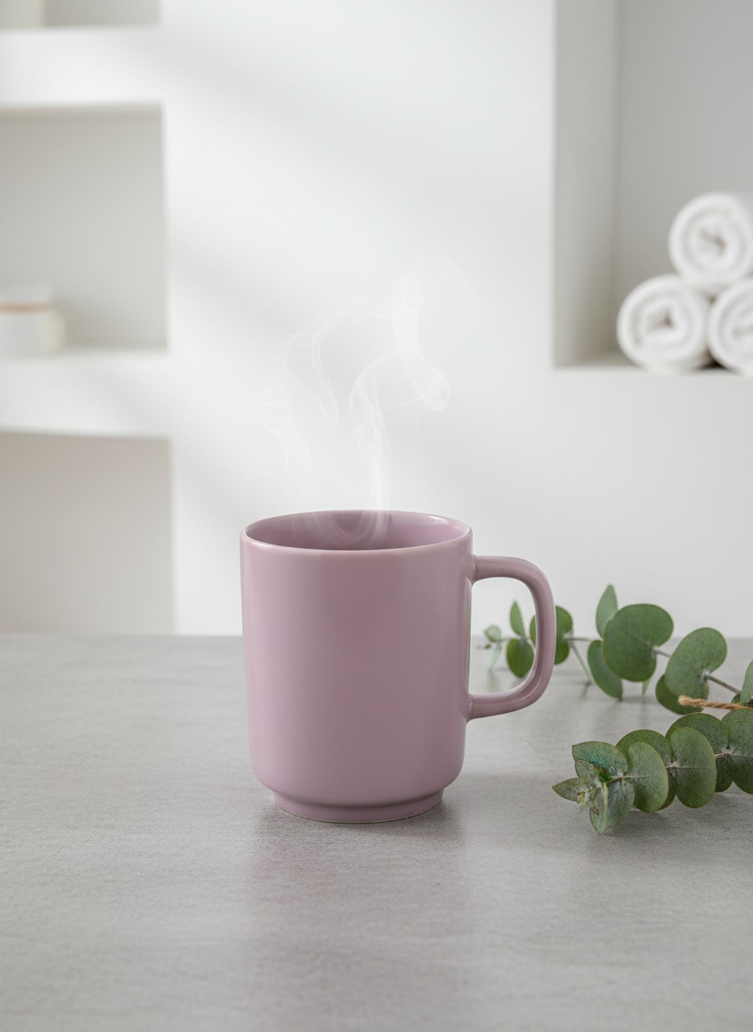 Elegant dusty rose ceramic coffee mug with steam on a stone tabletop with green eucalyptus accents.